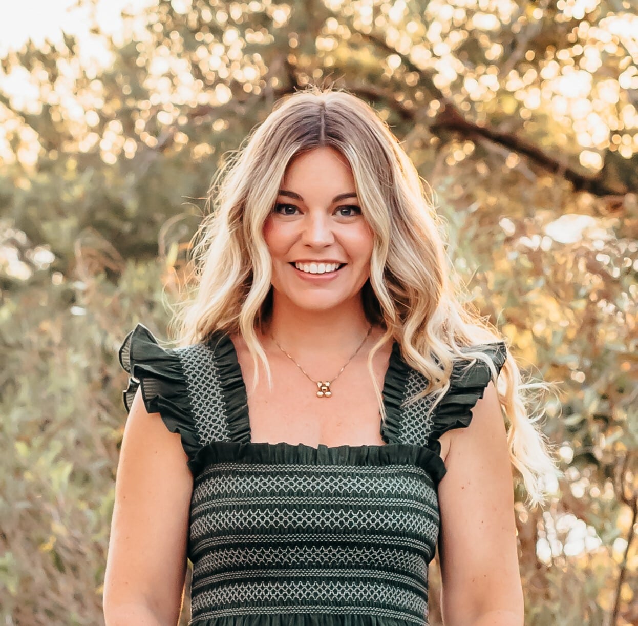 A smiling woman with long, wavy blond hair standing outdoors