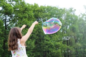 A young girl with brown hair holds up a large, iridescent bubble