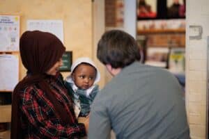 A mother wearing a head scarf holds an infant who is looking intently at another adult