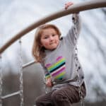 Young child wearing rainbow heart shirt and climbing on playground equipment