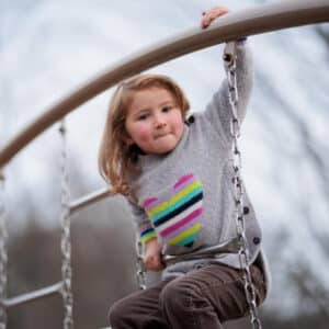 Young child wearing rainbow heart shirt and climbing on playground equipment