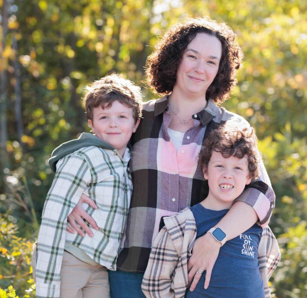 Sarah Morrison with her arms around her two young sons outdoors with trees in background