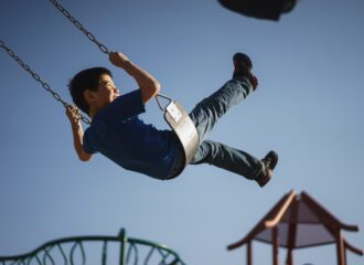 A young boy swings on a playground swing while smiling