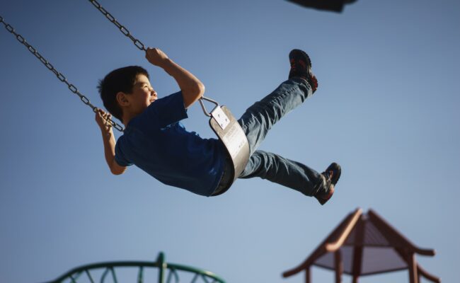 A young boy swings on a playground swing while smiling
