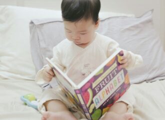 An Asian baby holds a picture book called Fruit Alphabet