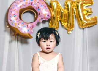 Young girl celebrating her first birthday with balloons spelling out "ONE"